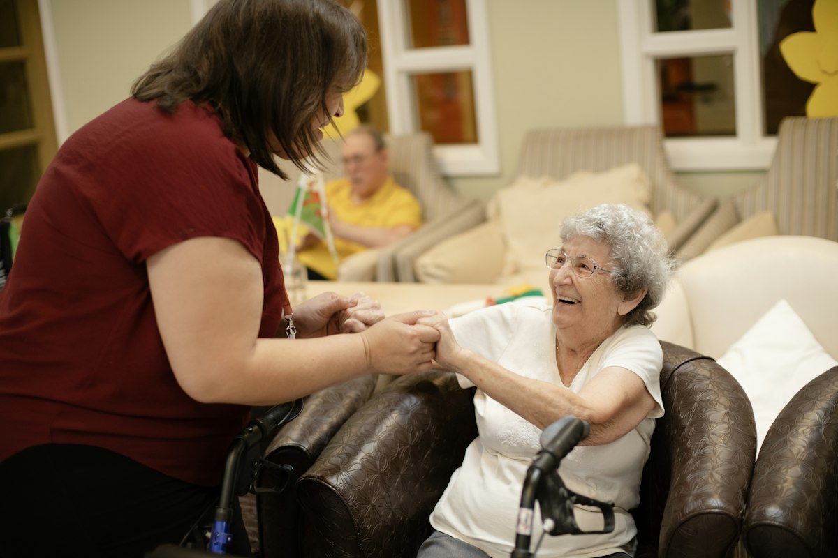 A caregiver helping an older woman stand up with her walker