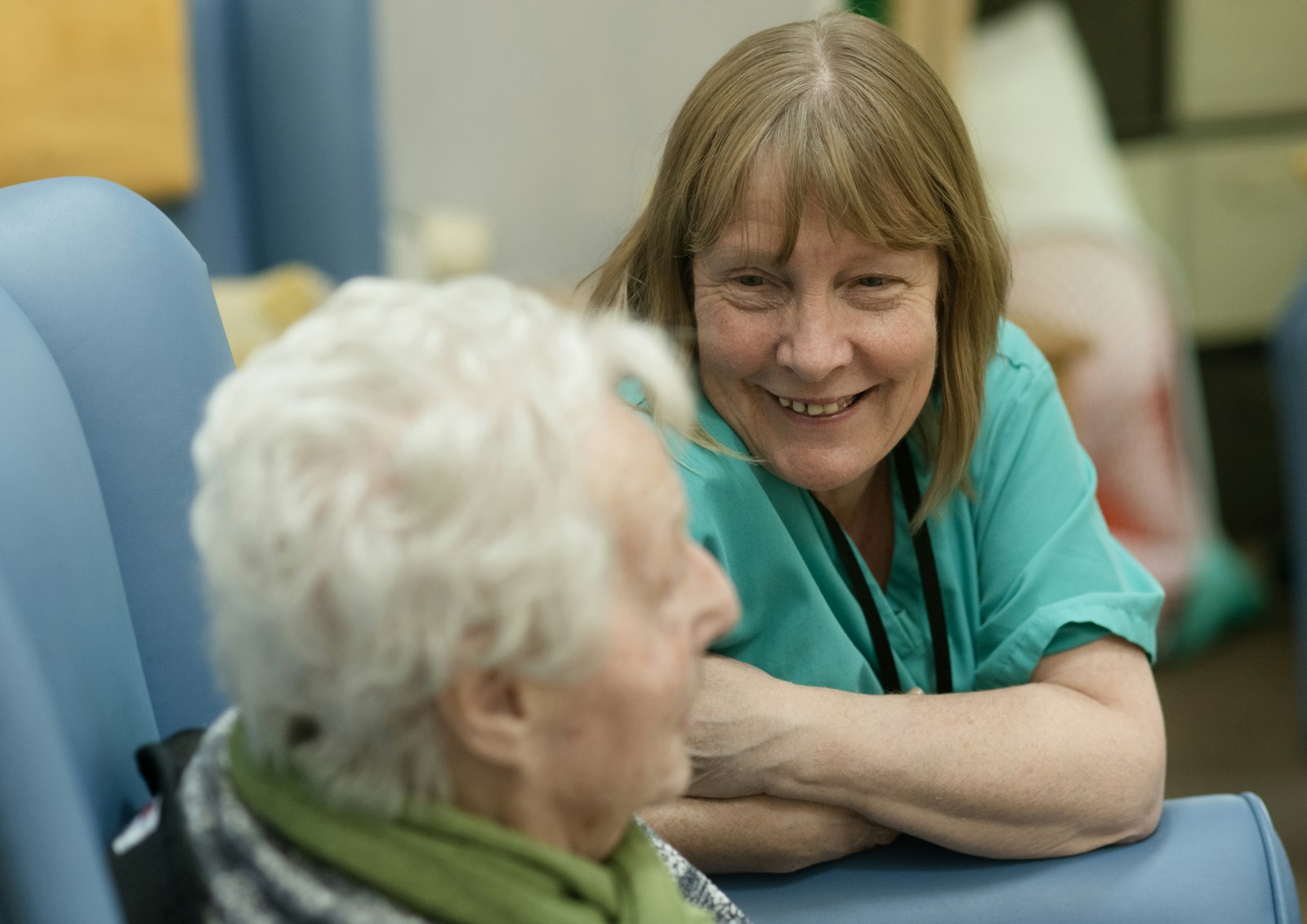 A nurse in scrubs talking with a senior woman