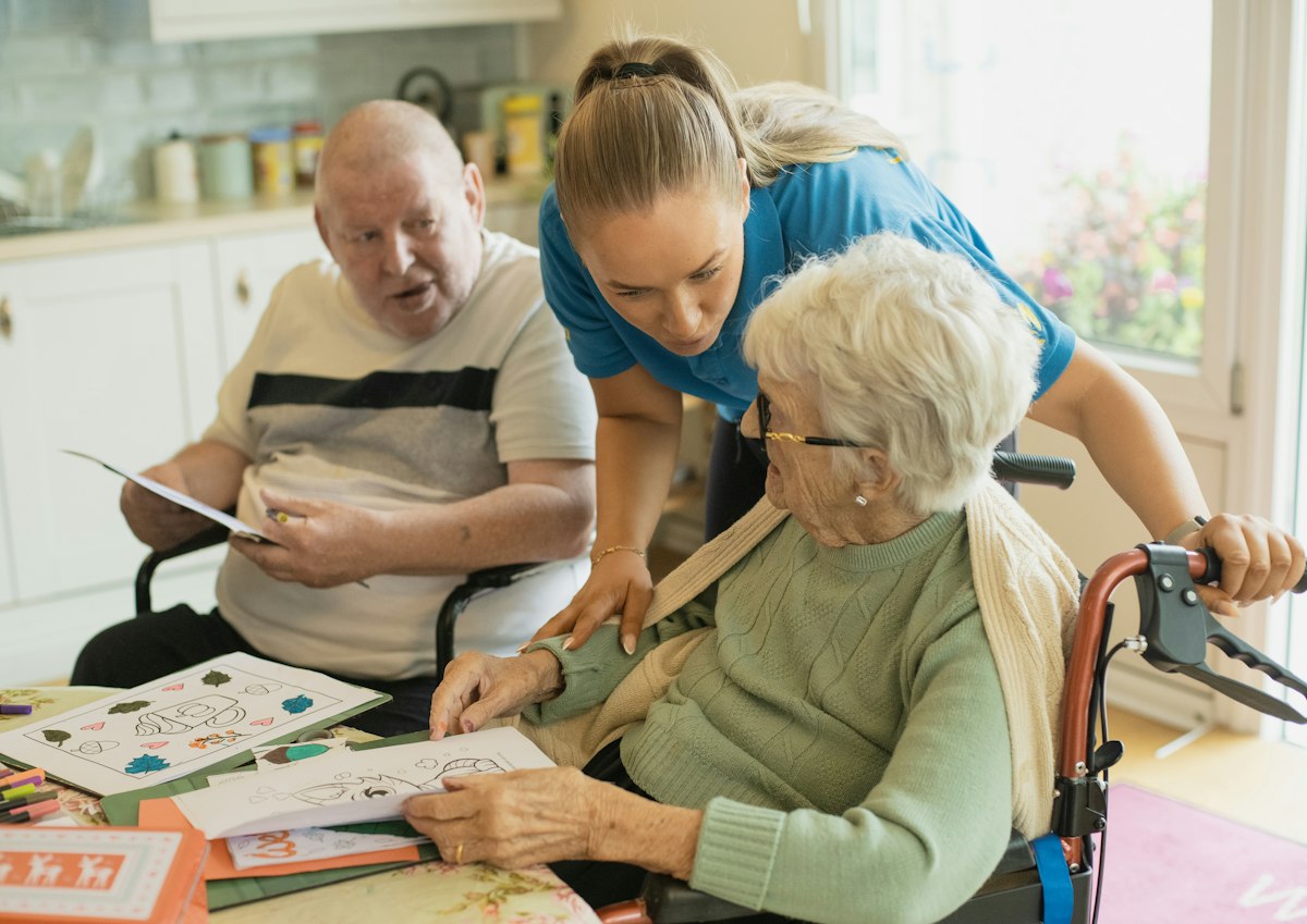 A caregiver helping an older couple with an activity at their kitchen table